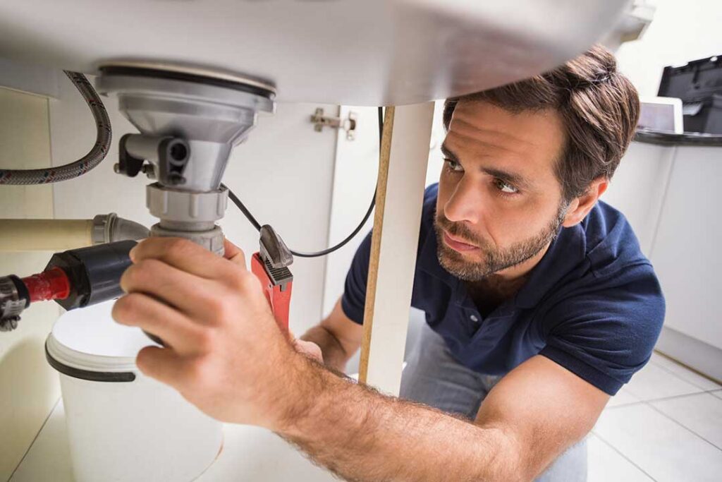A homeowner examining a water heater in a garage with visible water stains on the floor.