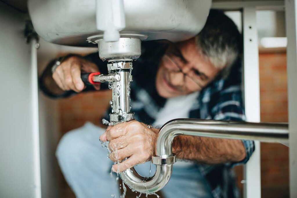 A plumber inspecting a wall-mounted tankless water heater in a residential utility room.